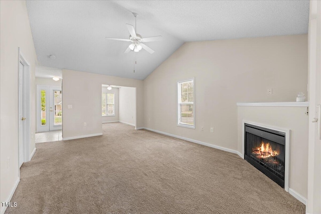 unfurnished living room featuring a ceiling fan, carpet floors, a warm lit fireplace, lofted ceiling, and baseboards
