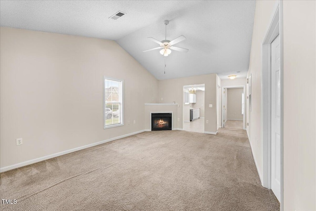 unfurnished living room with a ceiling fan, carpet, a warm lit fireplace, vaulted ceiling, and baseboards