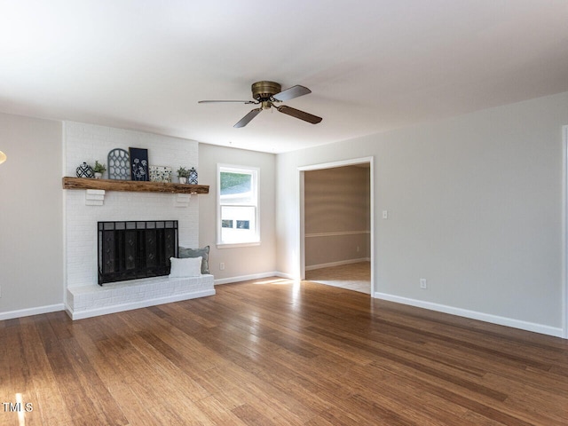 unfurnished living room featuring a brick fireplace, a ceiling fan, wood finished floors, and baseboards