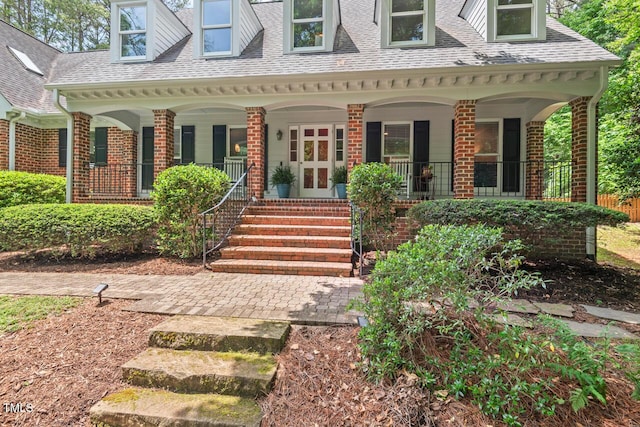 view of exterior entry with covered porch, brick siding, and roof with shingles
