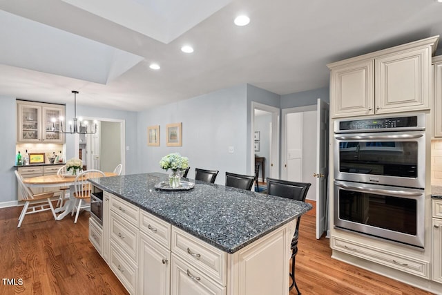 kitchen featuring stainless steel double oven, wood finished floors, recessed lighting, a breakfast bar area, and a kitchen island