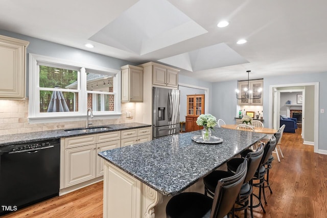 kitchen with dishwasher, stainless steel refrigerator with ice dispenser, a sink, cream cabinetry, and light wood-style floors