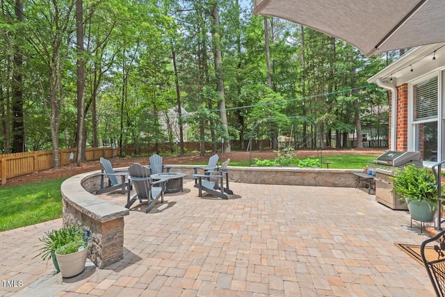 view of patio featuring an outdoor fire pit, a fenced backyard, grilling area, and view of scattered trees