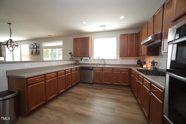 kitchen featuring stainless steel dishwasher, double wall oven, a sink, under cabinet range hood, and a peninsula