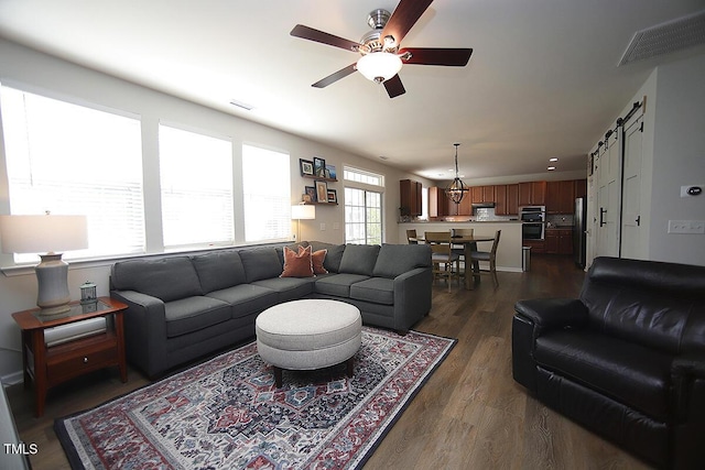 living room featuring a ceiling fan, a barn door, and dark wood-type flooring