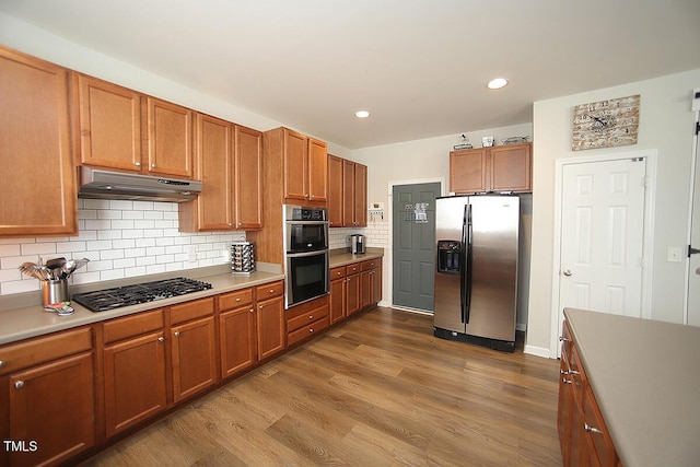 kitchen with appliances with stainless steel finishes, under cabinet range hood, dark wood-style flooring, decorative backsplash, and brown cabinets