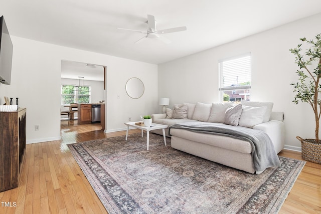 living area featuring light wood finished floors, ceiling fan, and baseboards