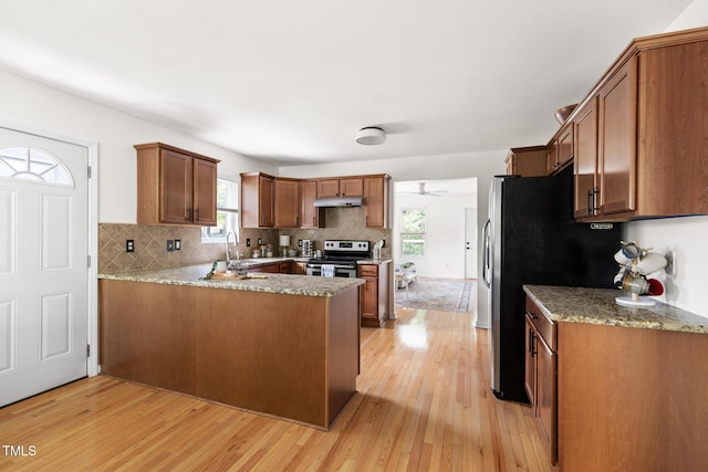 kitchen with appliances with stainless steel finishes, under cabinet range hood, a peninsula, light wood-type flooring, and decorative backsplash