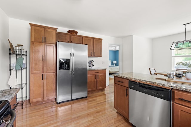 kitchen with stainless steel appliances, light wood-style flooring, brown cabinets, and light stone countertops