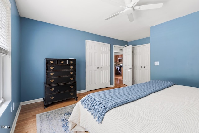 bedroom featuring wood finished floors, baseboards, multiple closets, and ceiling fan