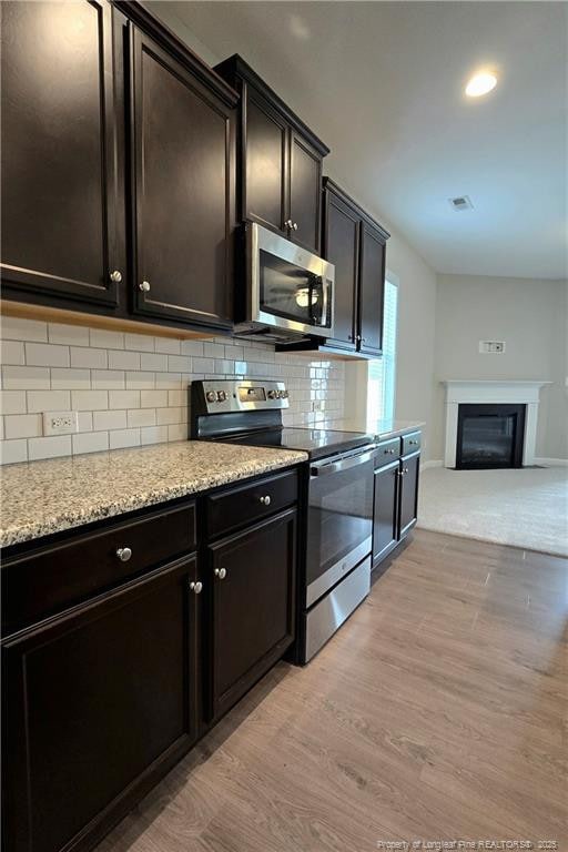 338 E David Parnell St, Parkton, NC 28371 - kitchen featuring stainless steel appliances, light wood-type flooring, decorative backsplash, open floor plan, and a glass covered fireplace