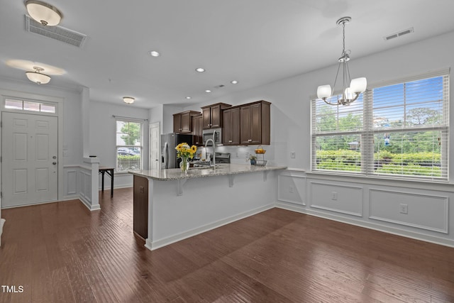 kitchen with stainless steel appliances, a peninsula, dark wood-style flooring, a chandelier, and light stone countertops