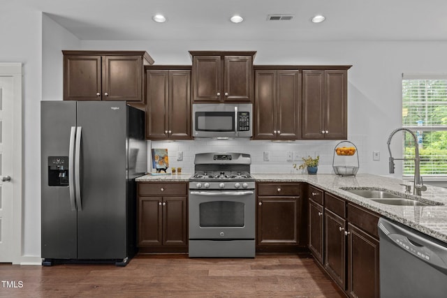 kitchen featuring appliances with stainless steel finishes, a sink, dark wood-style flooring, light stone countertops, and dark brown cabinetry