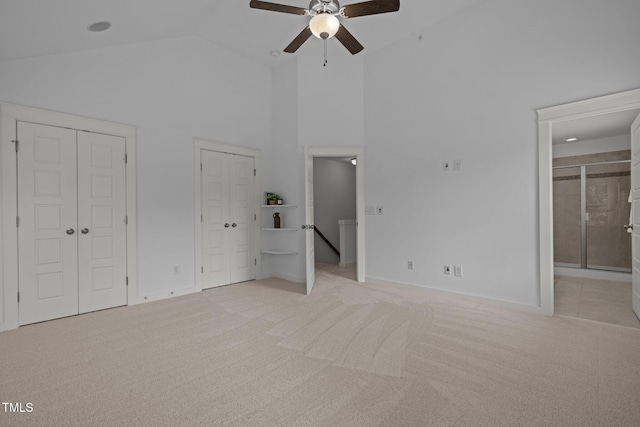 unfurnished bedroom with two closets, light colored carpet, high vaulted ceiling, connected bathroom, and baseboards