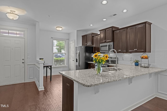 kitchen featuring stainless steel appliances, a sink, a kitchen breakfast bar, dark brown cabinets, and a peninsula