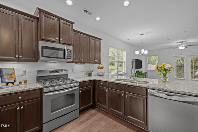 kitchen with stainless steel appliances, a sink, light wood finished floors, light stone counters, and dark brown cabinets