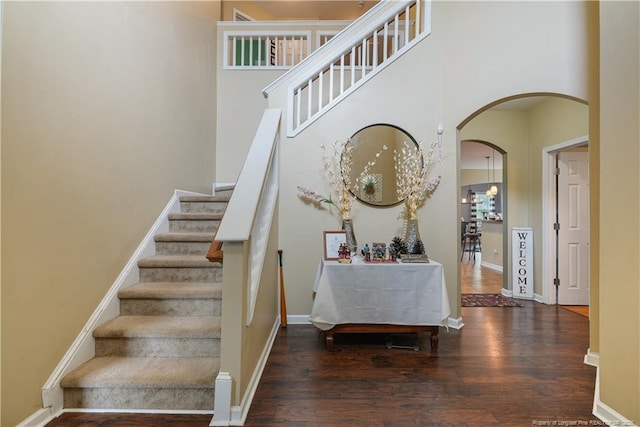 stairway with arched walkways, wood finished floors, baseboards, and a towering ceiling