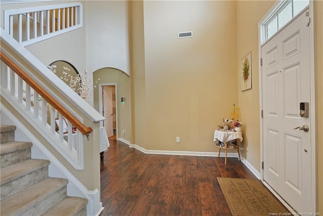 foyer with a high ceiling, dark wood-type flooring, baseboards, stairway, and arched walkways
