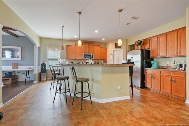 kitchen with appliances with stainless steel finishes, arched walkways, a breakfast bar, brown cabinets, and recessed lighting