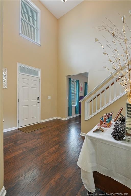 foyer entrance with stairway, dark wood-style flooring, baseboards, and a high ceiling