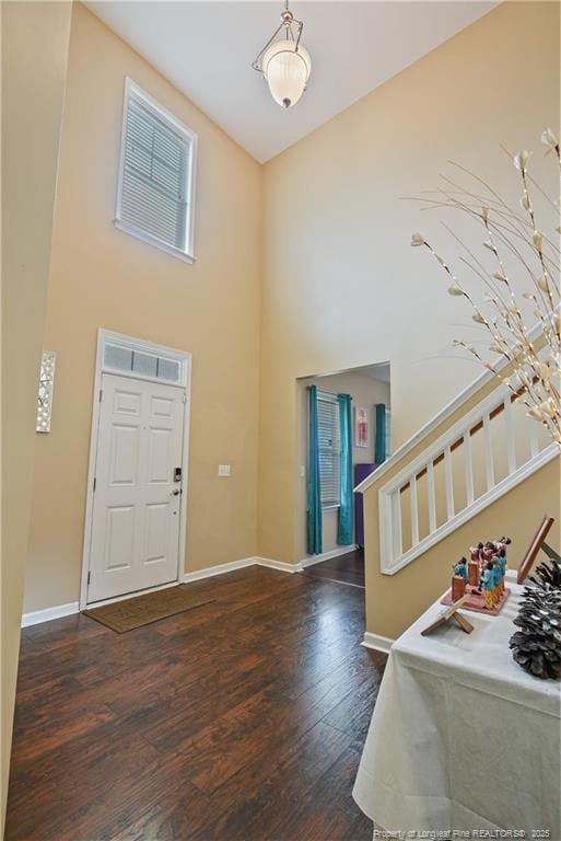 foyer entrance with stairs, dark wood-style floors, baseboards, and a high ceiling
