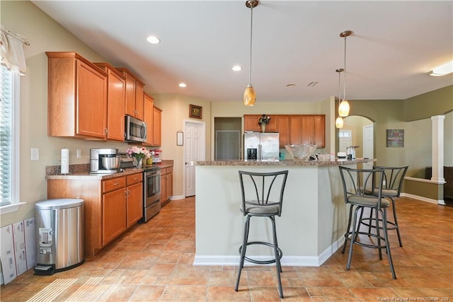 kitchen featuring appliances with stainless steel finishes, brown cabinetry, a breakfast bar, arched walkways, and recessed lighting