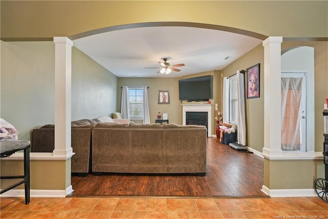 living area featuring ornate columns, ceiling fan, arched walkways, and baseboards