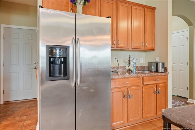 kitchen with stainless steel refrigerator with ice dispenser, arched walkways, brown cabinets, and light stone counters