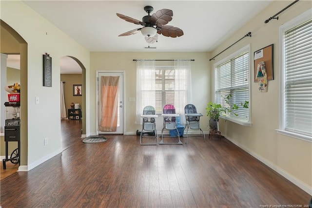 dining room with arched walkways, wood finished floors, a ceiling fan, and baseboards
