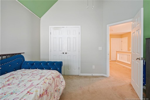 bedroom featuring light carpet, lofted ceiling, baseboards, and a closet