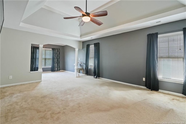 empty room featuring a tray ceiling, decorative columns, arched walkways, ceiling fan, and carpet