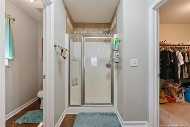 bathroom featuring a shower stall, toilet, a spacious closet, baseboards, and wood finished floors