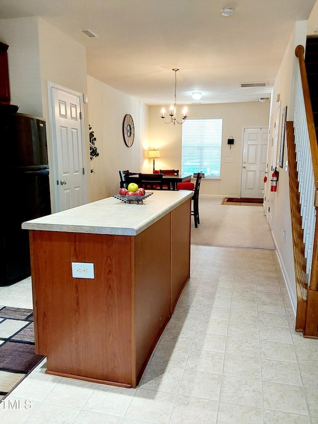 kitchen featuring freestanding refrigerator, a center island, light countertops, a chandelier, and pendant lighting