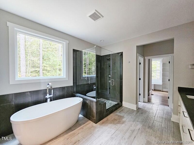 full bathroom featuring wood finished floors, a soaking tub, a stall shower, and vanity