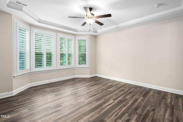 empty room featuring a raised ceiling, ceiling fan, baseboards, dark wood-type flooring, and ornamental molding