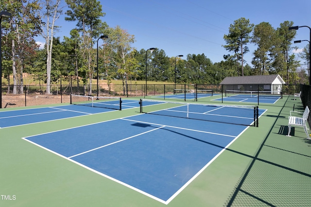 view of tennis court with community basketball court, fence, and view of scattered trees