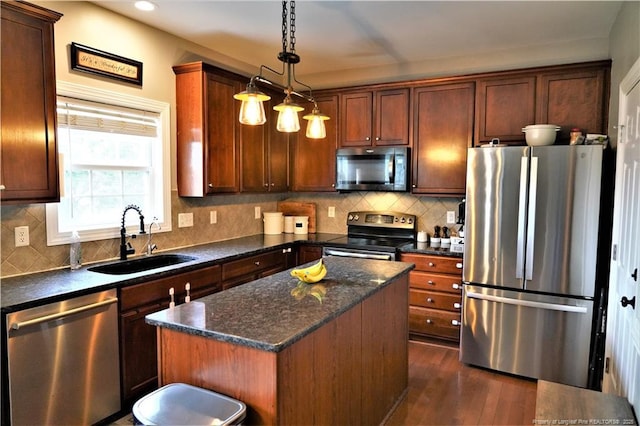 kitchen with appliances with stainless steel finishes, a sink, a kitchen island, dark wood-style flooring, and backsplash