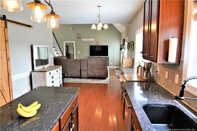 kitchen with a sink, wood finished floors, decorative light fixtures, dark stone counters, and lofted ceiling