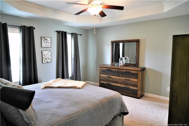 bedroom featuring a tray ceiling, crown molding, carpet flooring, baseboards, and a ceiling fan