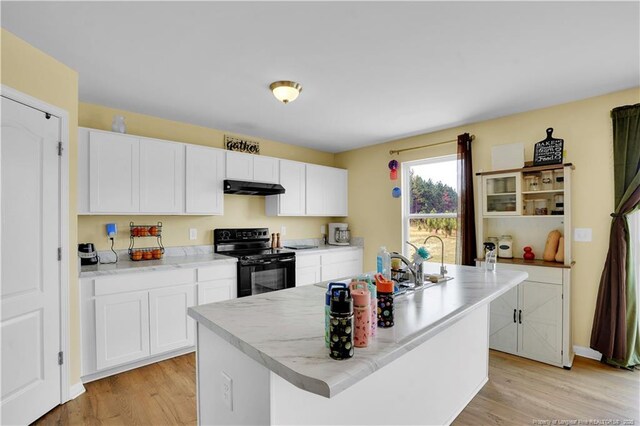 kitchen featuring black electric range oven, under cabinet range hood, white cabinets, light wood finished floors, and a center island with sink