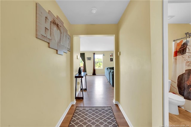 hallway featuring light wood finished floors and baseboards