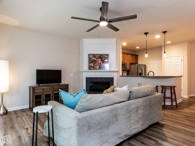 living area with ceiling fan, baseboards, dark wood-type flooring, a fireplace, and recessed lighting