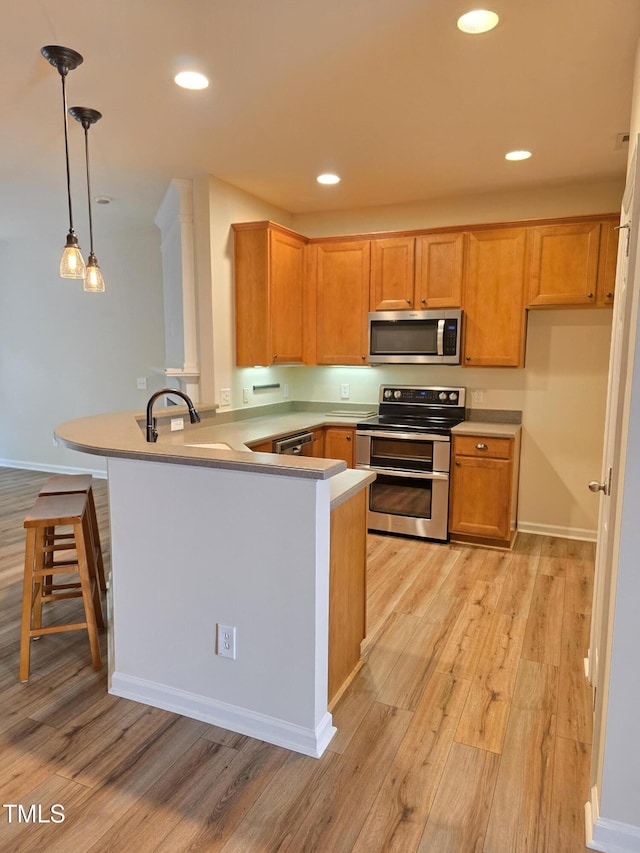 4206 Camden Woods Ct, Raleigh, NC 27612 - kitchen featuring stainless steel appliances, a peninsula, light wood-type flooring, hanging light fixtures, and light countertops