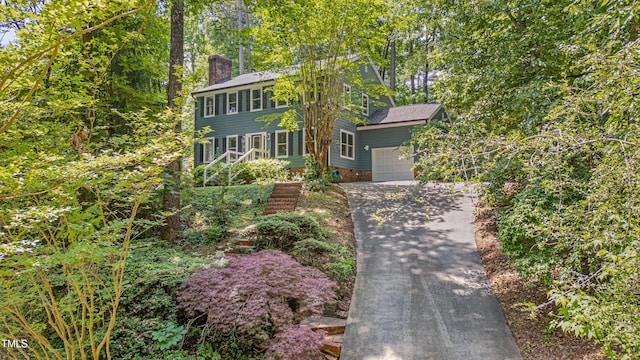 colonial-style house featuring a chimney, driveway, and an attached garage