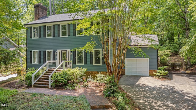 colonial home featuring a chimney, concrete driveway, fence, and a garage