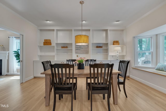dining room featuring crown molding, light wood finished floors, baseboards, and a fireplace