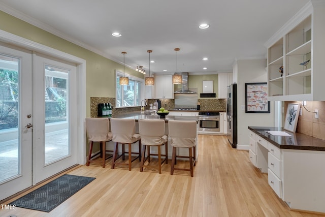 kitchen featuring wall chimney range hood, appliances with stainless steel finishes, a peninsula, decorative backsplash, and white cabinets