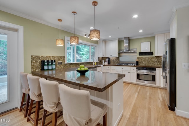 kitchen with stainless steel appliances, wall chimney exhaust hood, a peninsula, ornamental molding, and decorative backsplash