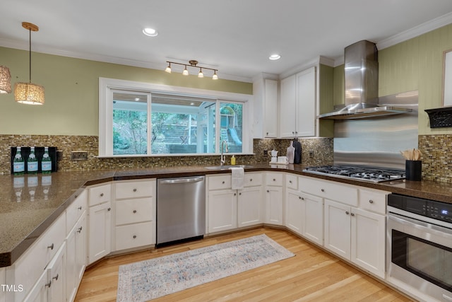 kitchen featuring stainless steel appliances, wall chimney range hood, a sink, ornamental molding, and light wood finished floors