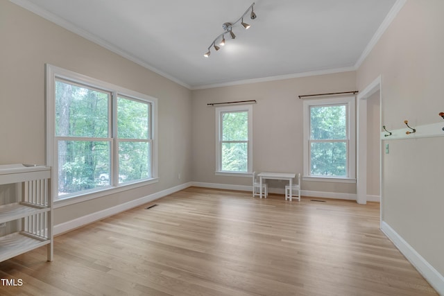 empty room featuring track lighting, light wood-style flooring, ornamental molding, and baseboards